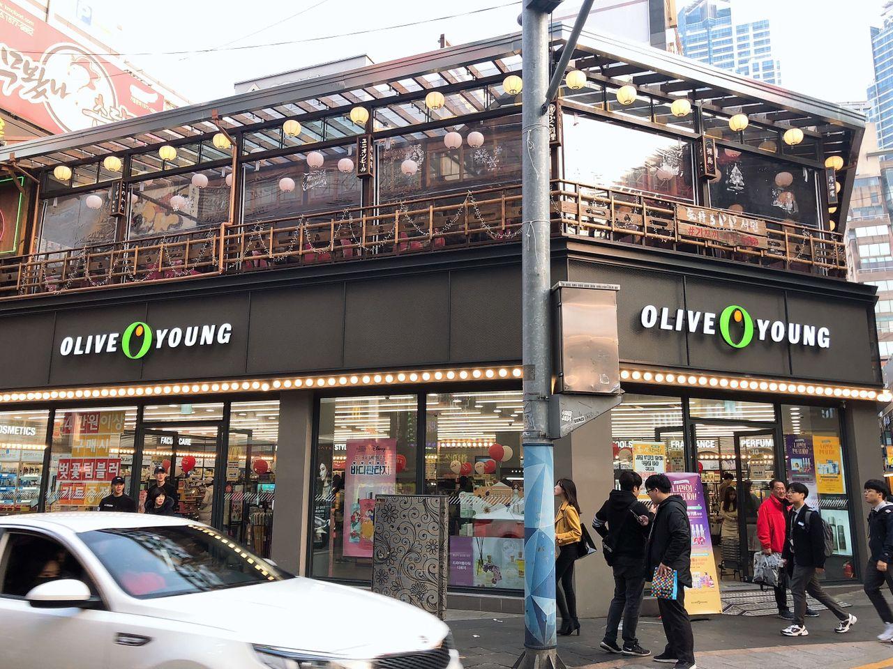 Olive Young在釜山西面购物商圈的大型店面，全景可见顾客在入口处活动。